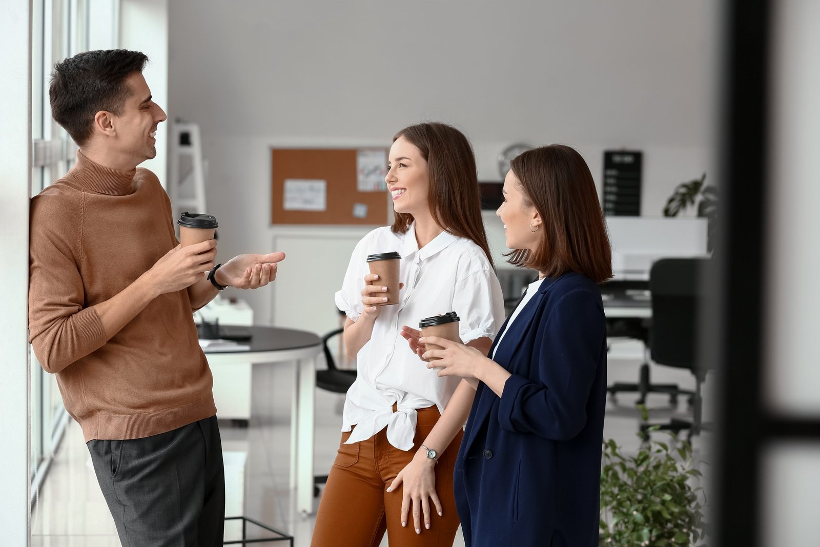 Drei Kollegen unterhalten sich lächelnd in der Kaffeepause im Büro – Sinnbild für ein positives Arbeitsklima durch Mitarbeiterbenefits.